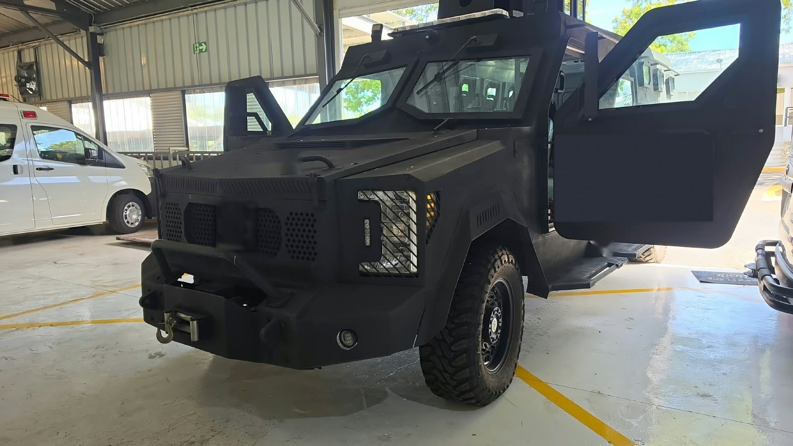 Vehículo táctico blindado de gran formato visto de frente, con las puertas abiertas dentro de una nave industrial
